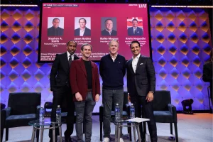 DraftKings and ESPN link sports betting to March Madness bracket contests. Stephen A. Smith, Jason Robins, Burke Magnus, and Kevin Negandhi pose on stage at the 2026 MIT Sloan Sports Analytics Conference during a panel on sports betting.